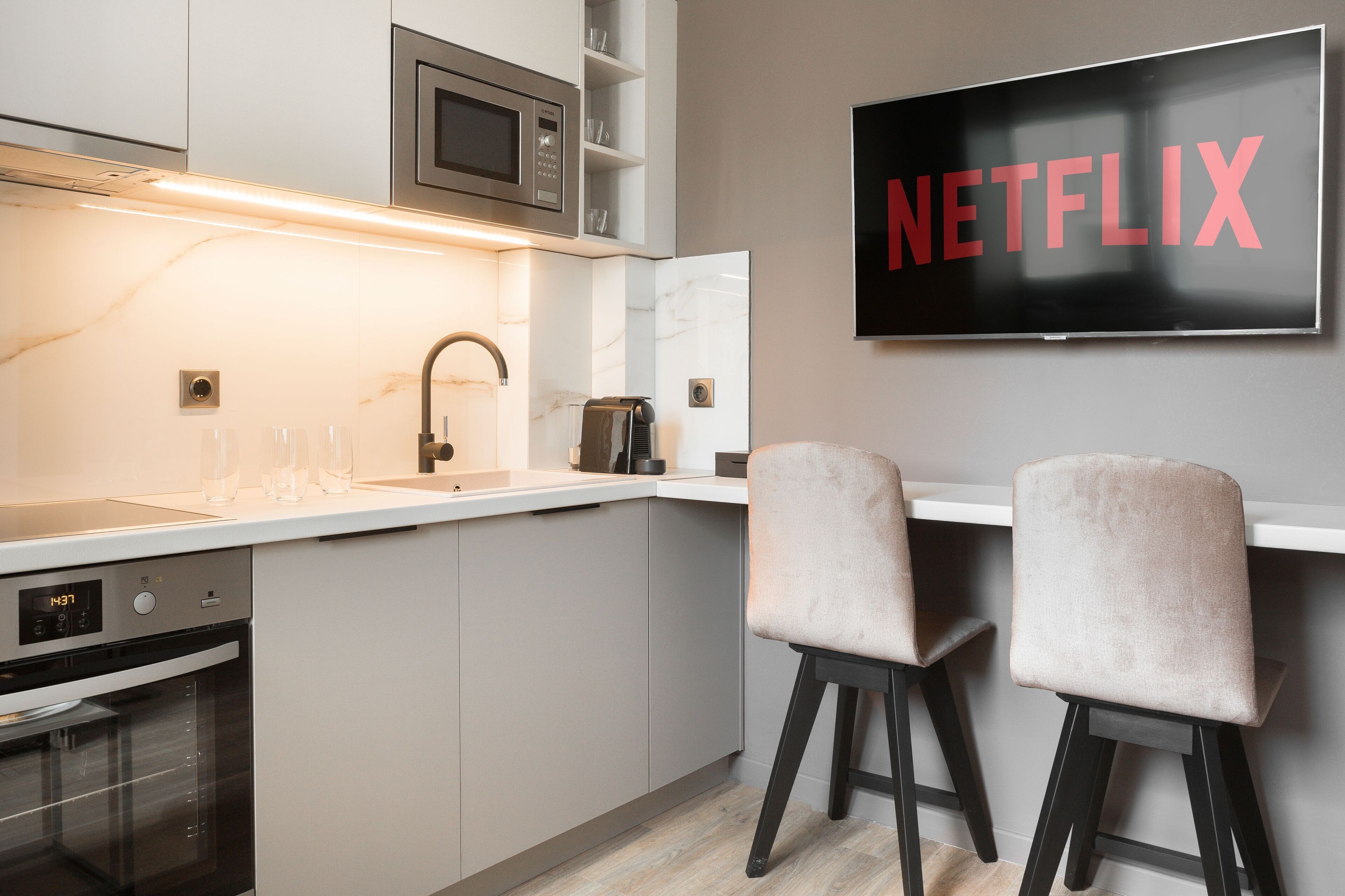 Moderni keittiö, jossa on sisäänrakennettu uuni, mikroaaltouuni ja pesuallas. Seinälle asennetussa taulutelevisiossa näkyy sana ”NETFLIX”.