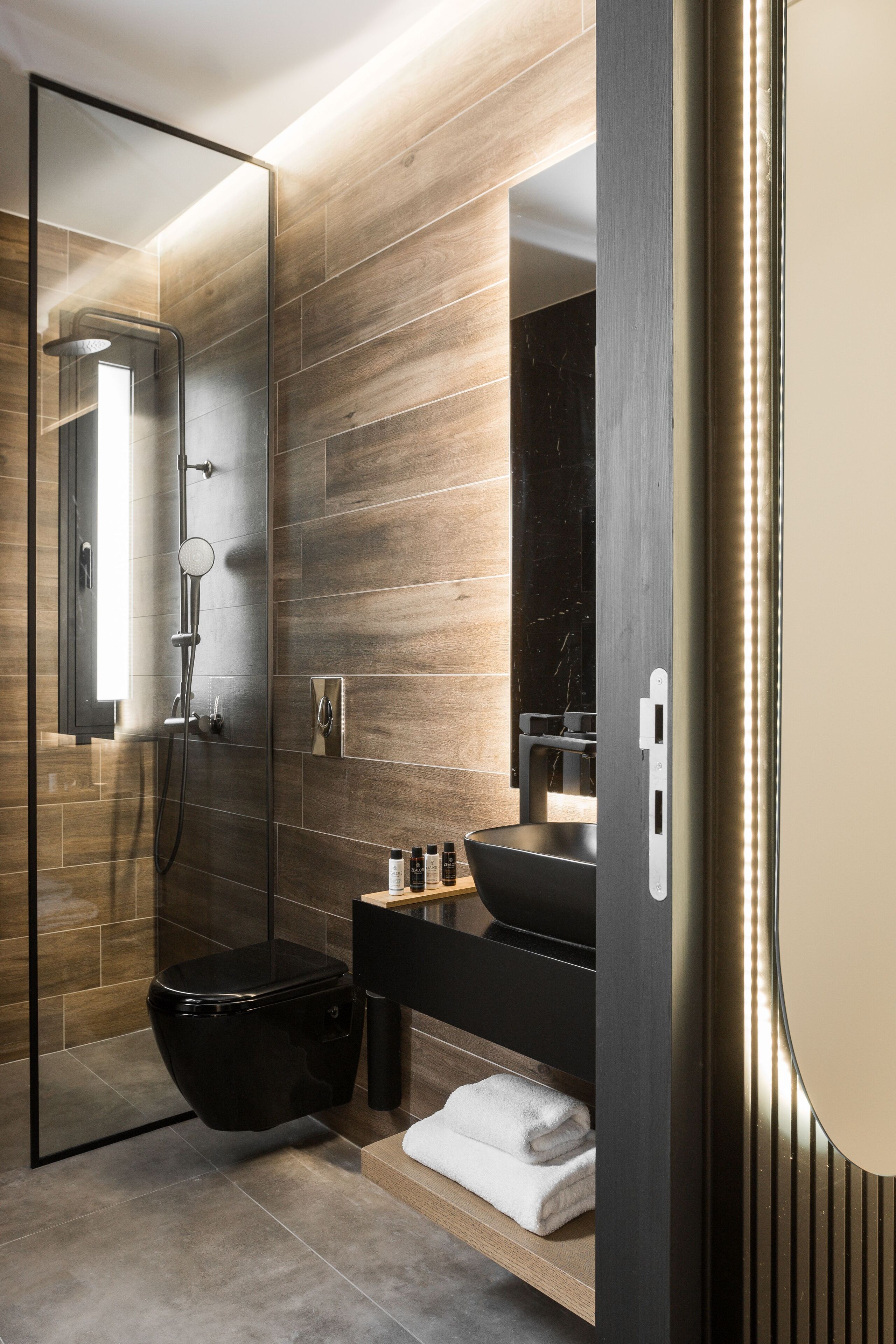 A modern bathroom with a glass-enclosed shower, a black sink, and a wooden vanity.