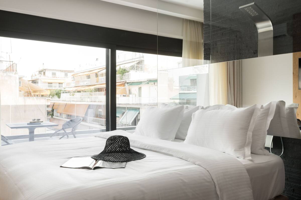 Une chambre d’hôtel avec un grand lit, une vue sur la ville et un balcon équipé d’une table et d’une chaise.