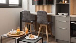 A modern kitchen with a built-in TV displaying "NETFLIX," a dining area with a table set for two, and a cozy seating area with a sofa. - LUX&EASY Athens Downtown Apartments (Athens)