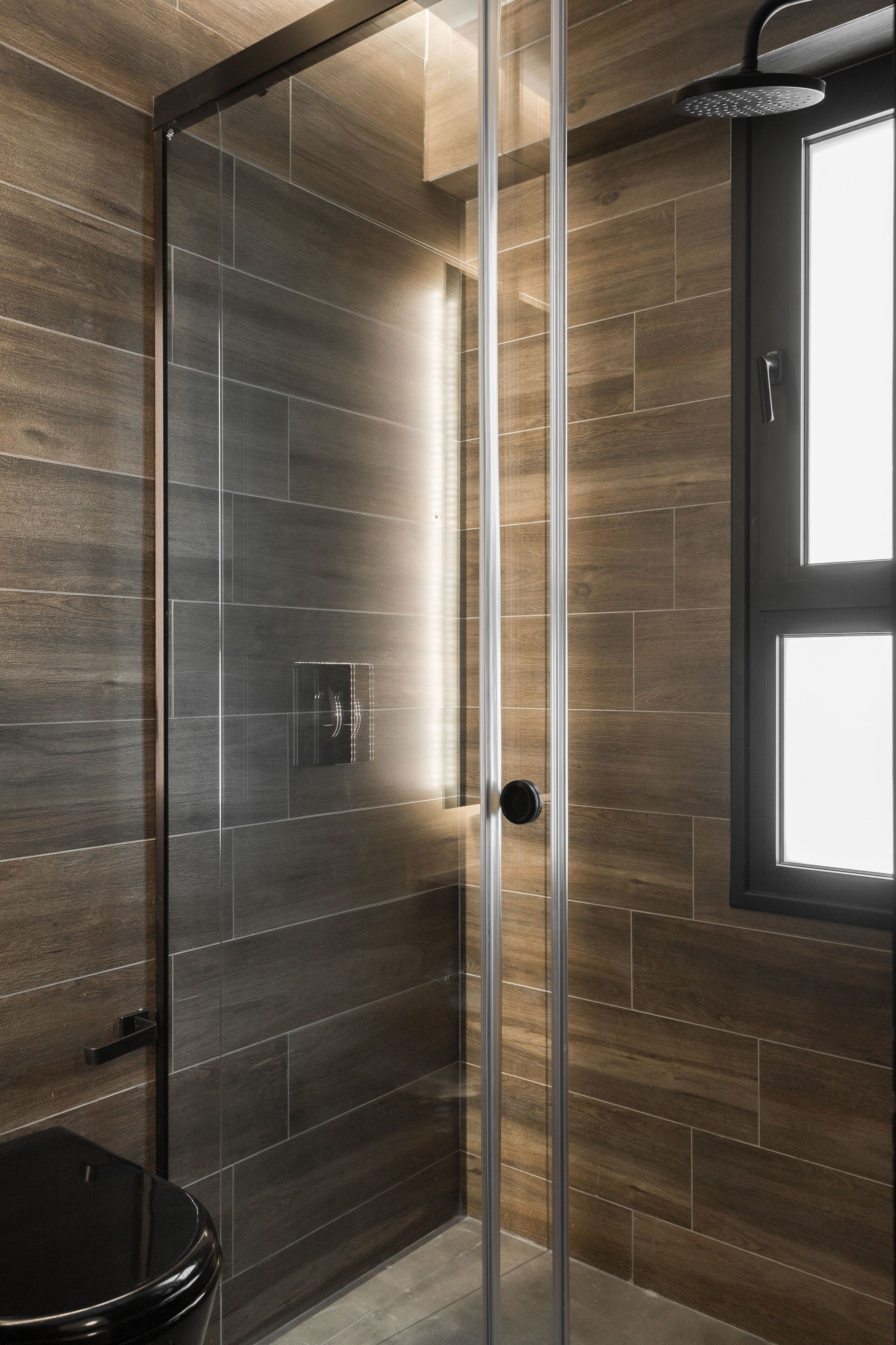 A modern bathroom with a glass shower enclosure, dark wood paneling, and a visible toilet.