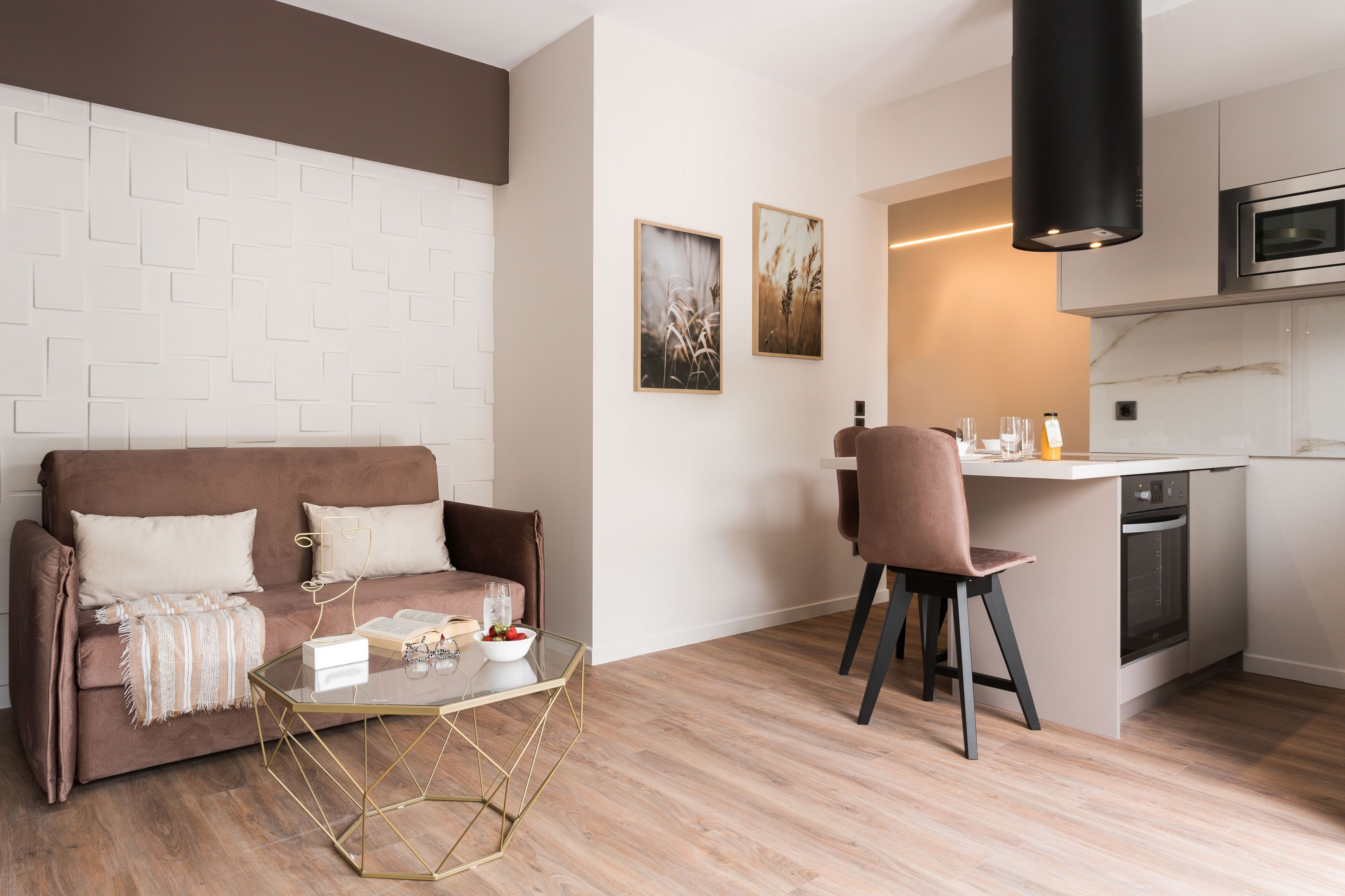 A modern living room with a brown sofa, a glass coffee table, and a kitchen area with a microwave and oven.