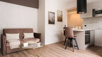 A modern living room with a brown sofa, a glass coffee table, and a kitchen area with a microwave and oven.