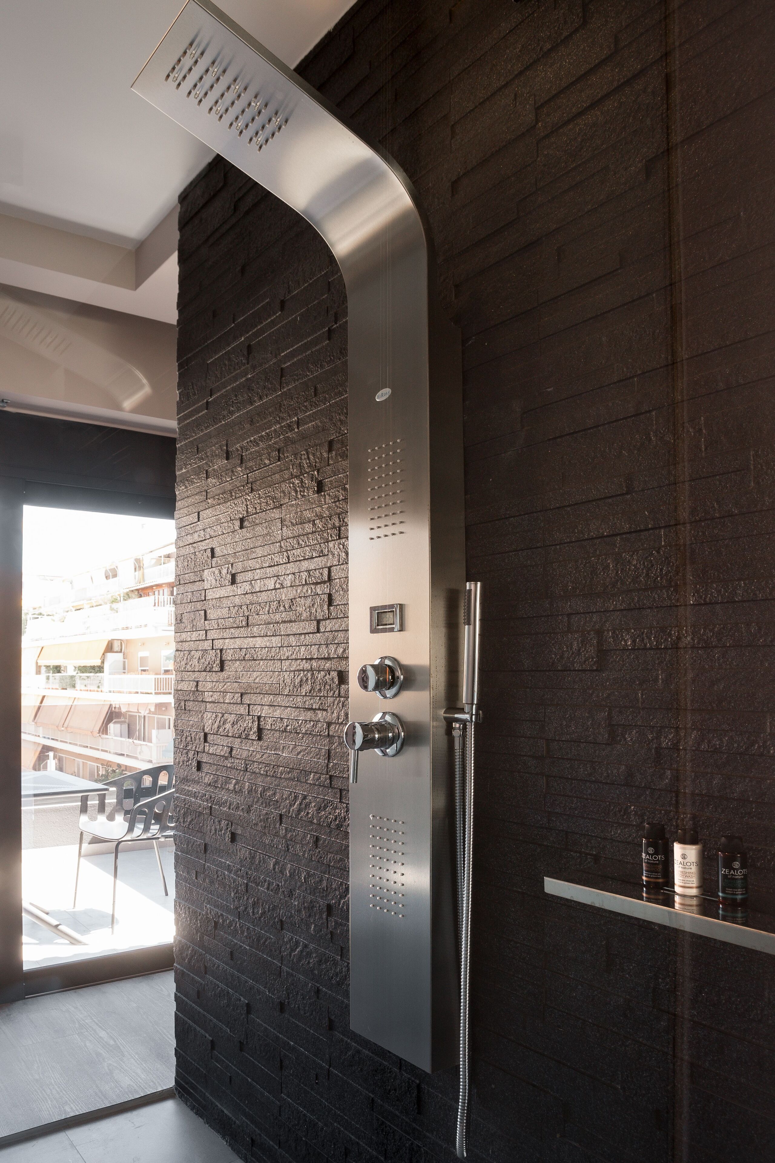 A modern bathroom with a curved shower head, a glass shelf with toiletries, and a view of the outside through a large window.