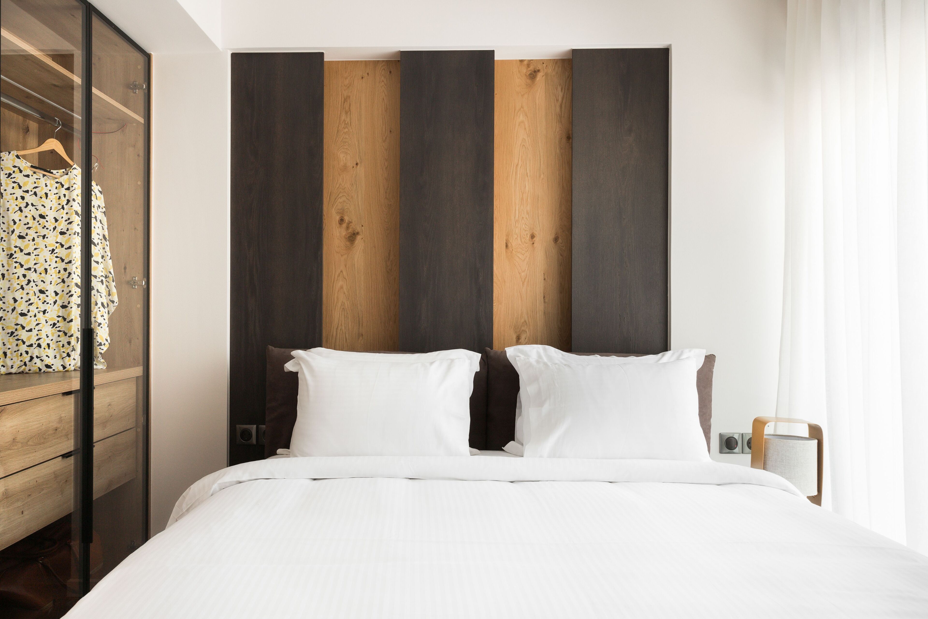 A modern hotel room with a large bed, wooden headboard, and a wooden wardrobe.