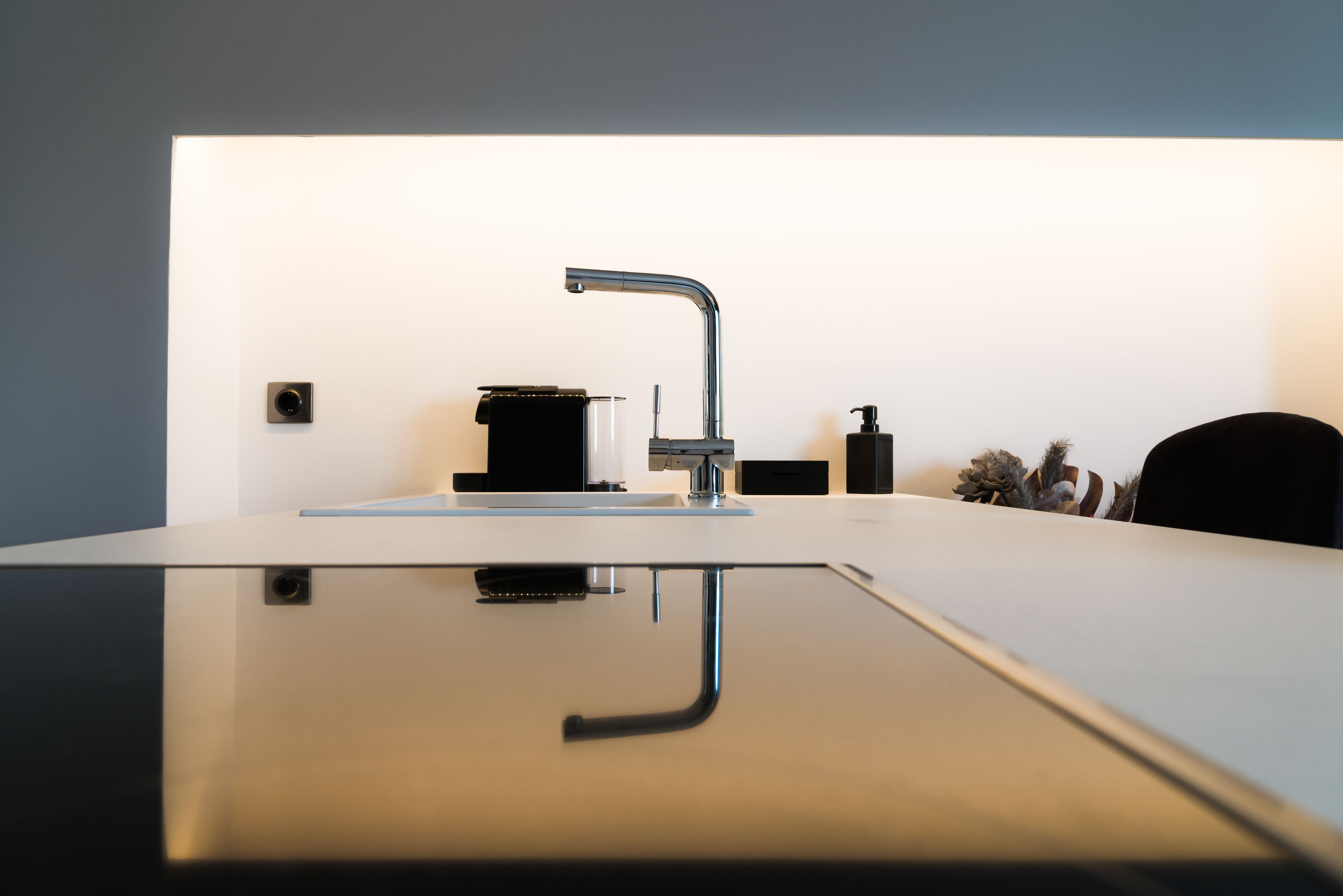Een moderne keuken met een strakke kraan, een koffieapparaat en een kleine plant.