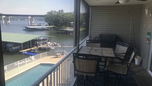 A balcony with a view of a dock and boats, a pool, and a table with chairs. - Can't Beat the View! (Camdenton)