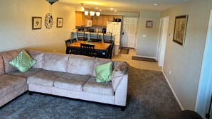 A living room with a beige sectional sofa, a ceiling fan, and a kitchen in the background. - Can't Beat the View! (Camdenton)