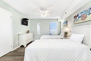 A bedroom with two beds, a ceiling fan, a TV mounted on the wall, and artwork on the wall.