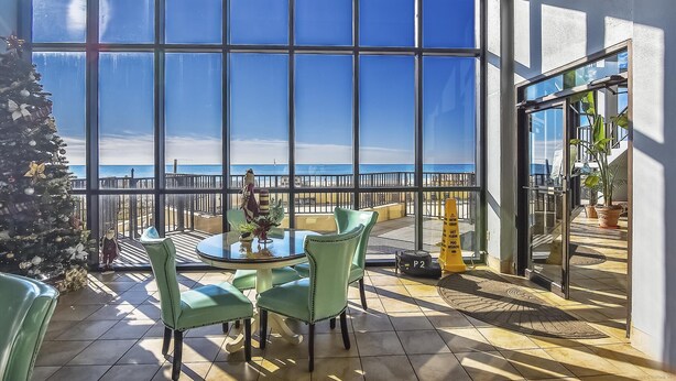 A balcony with a view of the ocean, furnished with green chairs and a table, and a Christmas tree.
