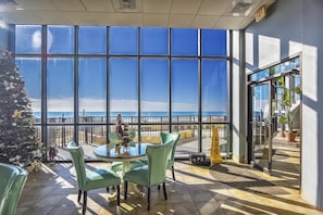 A terrace with a view of the ocean, featuring a round table and chairs, a Christmas tree, and a wet floor sign.