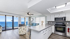 A modern kitchen with a large island, white cabinets, and a view of the ocean.