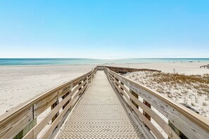 A wooden boardwalk leading to a beach with a clear sky.