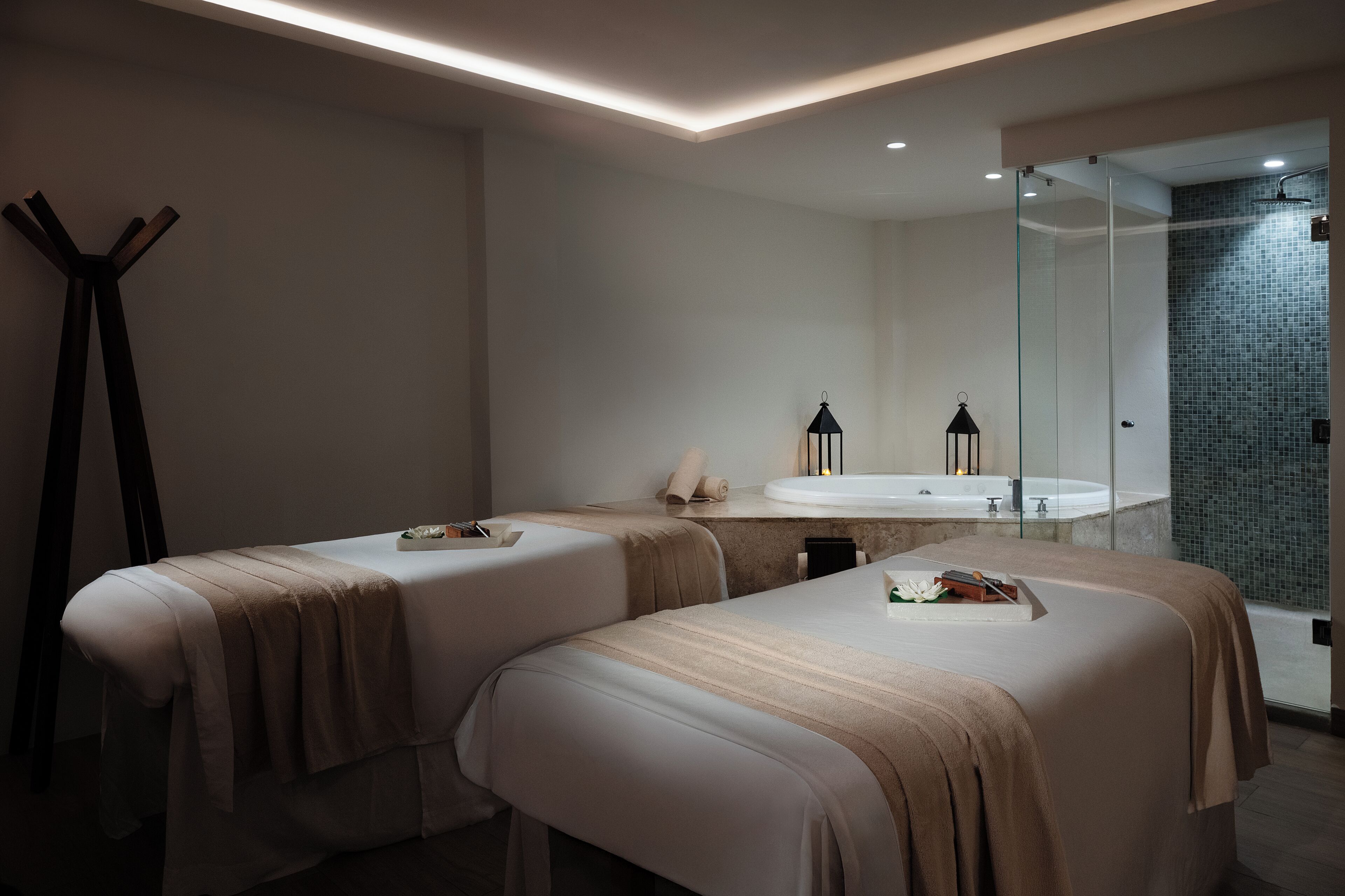 Una moderna sala spa con due lettini da massaggio, una doccia vetrata e un ampio specchio.