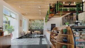 A modern interior with a wooden ceiling, a seating area with tables and chairs, a counter with a display case, and a wall with a tropical leaf pattern. - Dreams Puerto Morelos Resort & Spa - All Inclusive (Puerto Morelos)