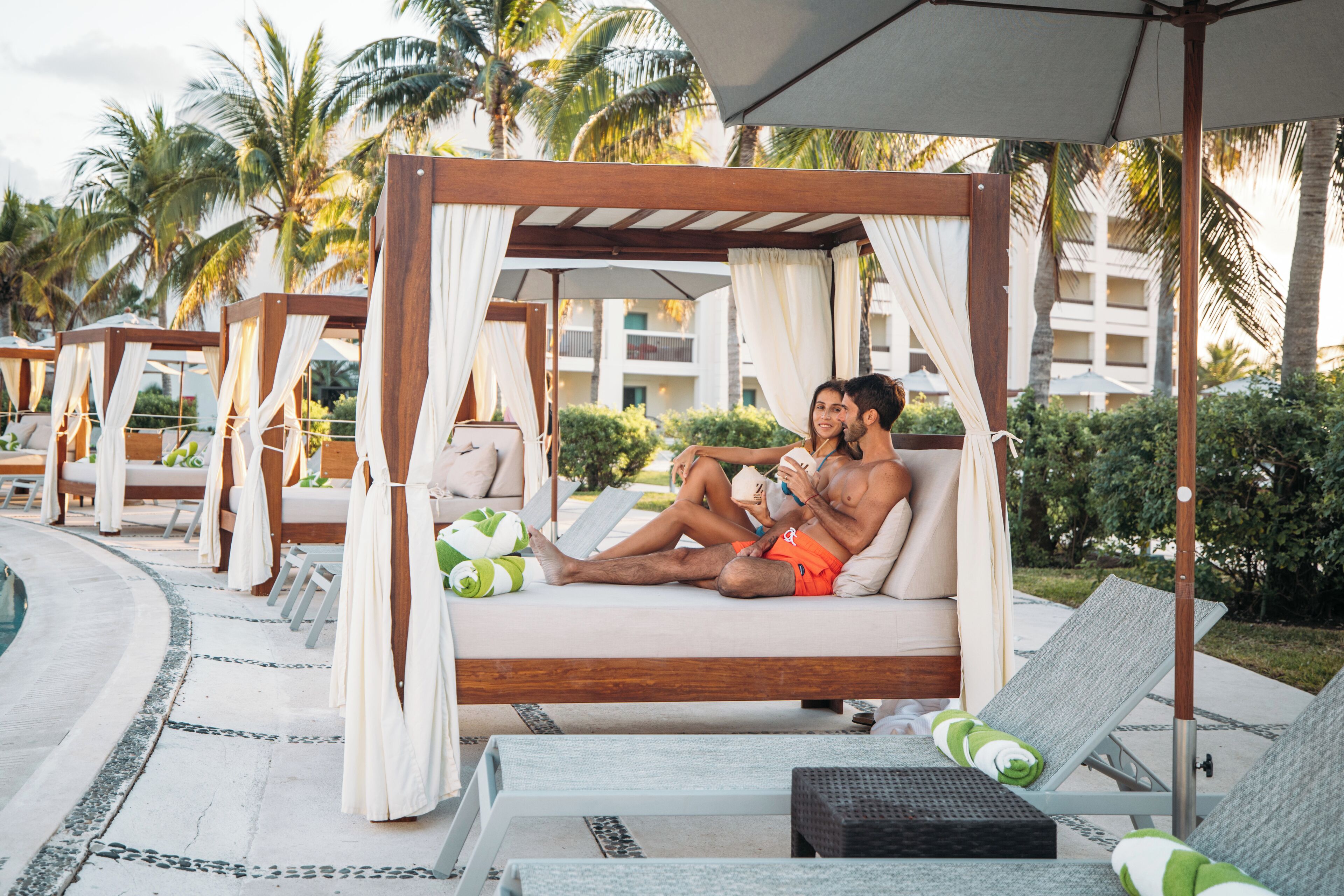 A poolside area with a wooden canopy bed, lounge chairs, and a pool.