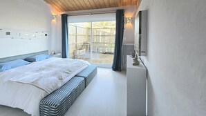 A bedroom with a large bed, a wooden ceiling, a sliding glass door to an outdoor area, and a wall-mounted TV.