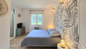 A bedroom with a bed, a television, a window, and a wall with a botanical print.