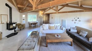 A spacious living area with a high wooden ceiling, a central sofa, a coffee table, and a fireplace.