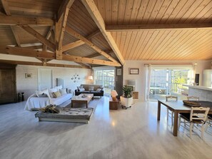 A spacious living area with a high ceiling, wooden beams, a sofa set, a dining table with chairs, and a view through large windows. - Charming house with private pool and WiFi in Dordogne (Montagrier)