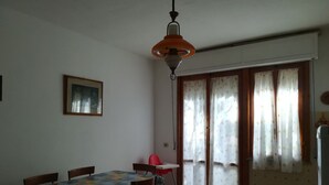 A dining area with a table and chairs, a hanging light fixture, a framed picture on the wall, and a sliding glass door with curtains.