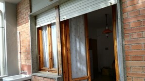 A room with a brick wall, a window with wooden shutters, a white sink, and a green gas cylinder.