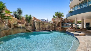 Une piscine aux eaux cristallines, entourée d’un paysage rocheux, et un bâtiment moderne doté de balcons.