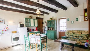 A cozy kitchen with a dining area, featuring wooden beams, green cabinets, and a patterned sofa.