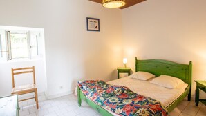 A bedroom with a green bed, a wooden chair, a window, and a hanging light fixture.
