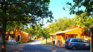 Una hilera de cabañas de madera con caminos de grava, mobiliario exterior y un coche estacionado.