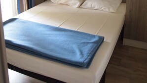 Una cama con una manta azul, paneles de madera en la pared y un cabecero blanco.