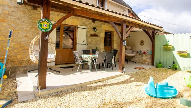 En bygning i sten med en overdækket patio, udendørs møbler og et skilt, der viser, at den er en del af Gites de France.
