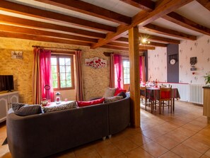 A cozy living room with a sectional sofa, a dining table with chairs, and a kitchen area in the background.