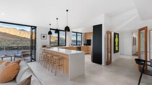 A modern kitchen with a large island, bar stools, and a view of mountains through large windows. - Oliver's Oasis | Luxury home | Spa Pool | BBQ | Fire (Queenstown)