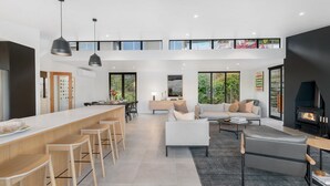 A modern open-plan living space with a kitchen, dining area, and seating area, featuring large windows and a fireplace. - Oliver's Oasis | Luxury home | Spa Pool | BBQ | Fire (Queenstown)