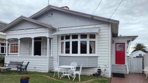 A single-story house with a front porch, a red door, and a small garden area with a bench and a table. - ✨3 Bdrm Guest Suite in 1920s Bungalow, North Shore (Auckland)