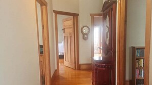 A hallway with wooden flooring, a wooden door, a clock on the wall, and a bookshelf. - ✨3 Bdrm Guest Suite in 1920s Bungalow, North Shore (Auckland)