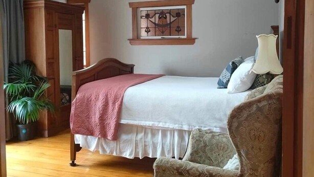 A bedroom with a wooden bed, a chair, a chandelier, and a window with a decorative frame. - ✨3 Bdrm Guest Suite in 1920s Bungalow, North Shore (Auckland)