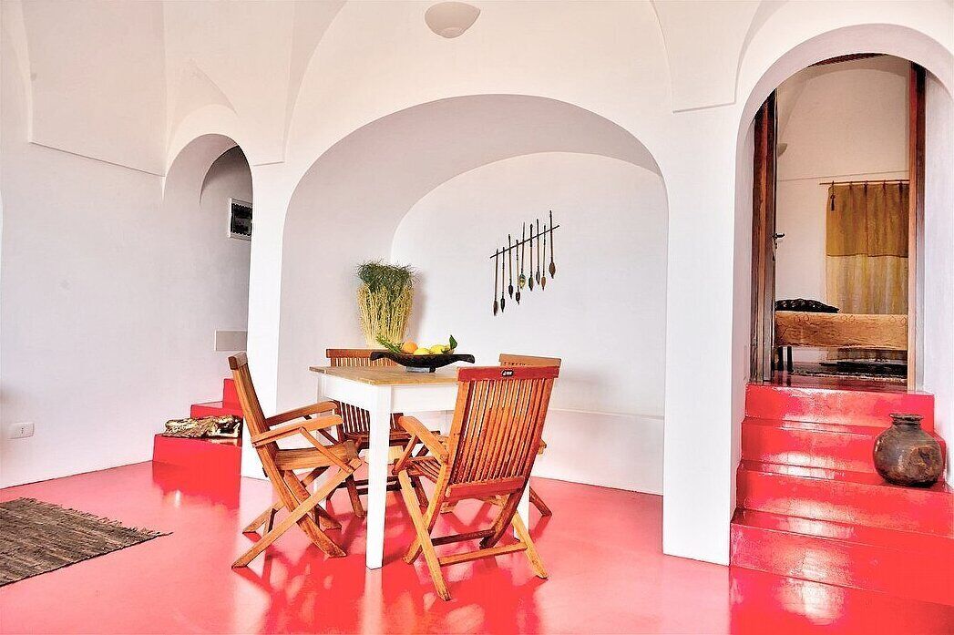 A dining area with a white table and wooden chairs, a hanging plant, and a wall-mounted decorative piece.
