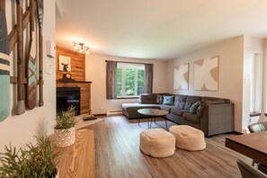 A cozy living room with a fireplace, a sofa, a coffee table, and a dining area. - Townhouse on the Golf w/ Pool Access -Aiglon 1717 (Mont-Tremblant)