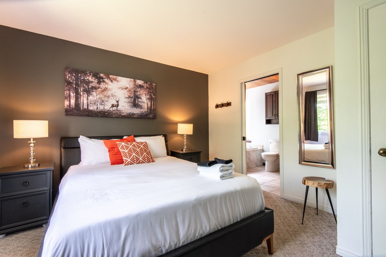 A bedroom with a large bed, two bedside lamps, a painting on the wall, and a view into the bathroom.