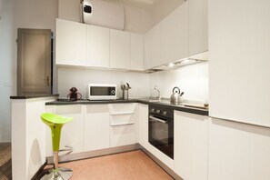 A modern kitchen with white cabinets, a black countertop, a microwave, a kettle, and a green bar stool.