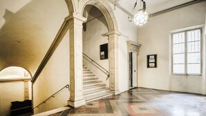A spacious interior with a grand staircase, a chandelier, and a large window allowing natural light. - UR-NEST Monte Grappa (Bologna)
