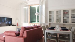 A modern living room with a red sofa, a dining table set for four, and a TV mounted on the wall. - UR-NEST Monte Grappa (Bologna)