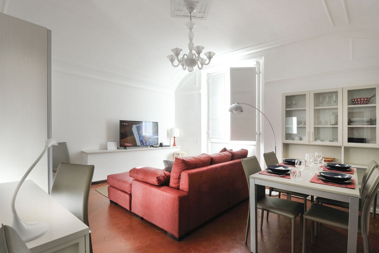 Un salon moderne avec un canapé rouge, une table à manger dressée pour quatre personnes et un téléviseur posé sur un meuble blanc.