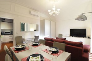 A modern living room with a dining area, a flat-screen TV, and a chandelier. - UR-NEST Monte Grappa (Bologna)