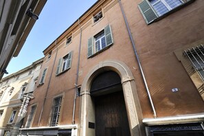 A building with a brown facade, multiple windows with shutters, and a prominent arched entrance.