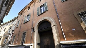 A building with a brown facade, multiple windows with shutters, and a prominent arched entrance. - UR-NEST Monte Grappa (Bologna)