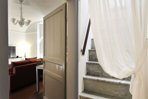 A staircase with a white curtain, a wooden door, and a red sofa in the background.