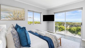 Un dormitorio con una cama grande, un televisor montado en la pared y un balcón con vistas al paisaje.